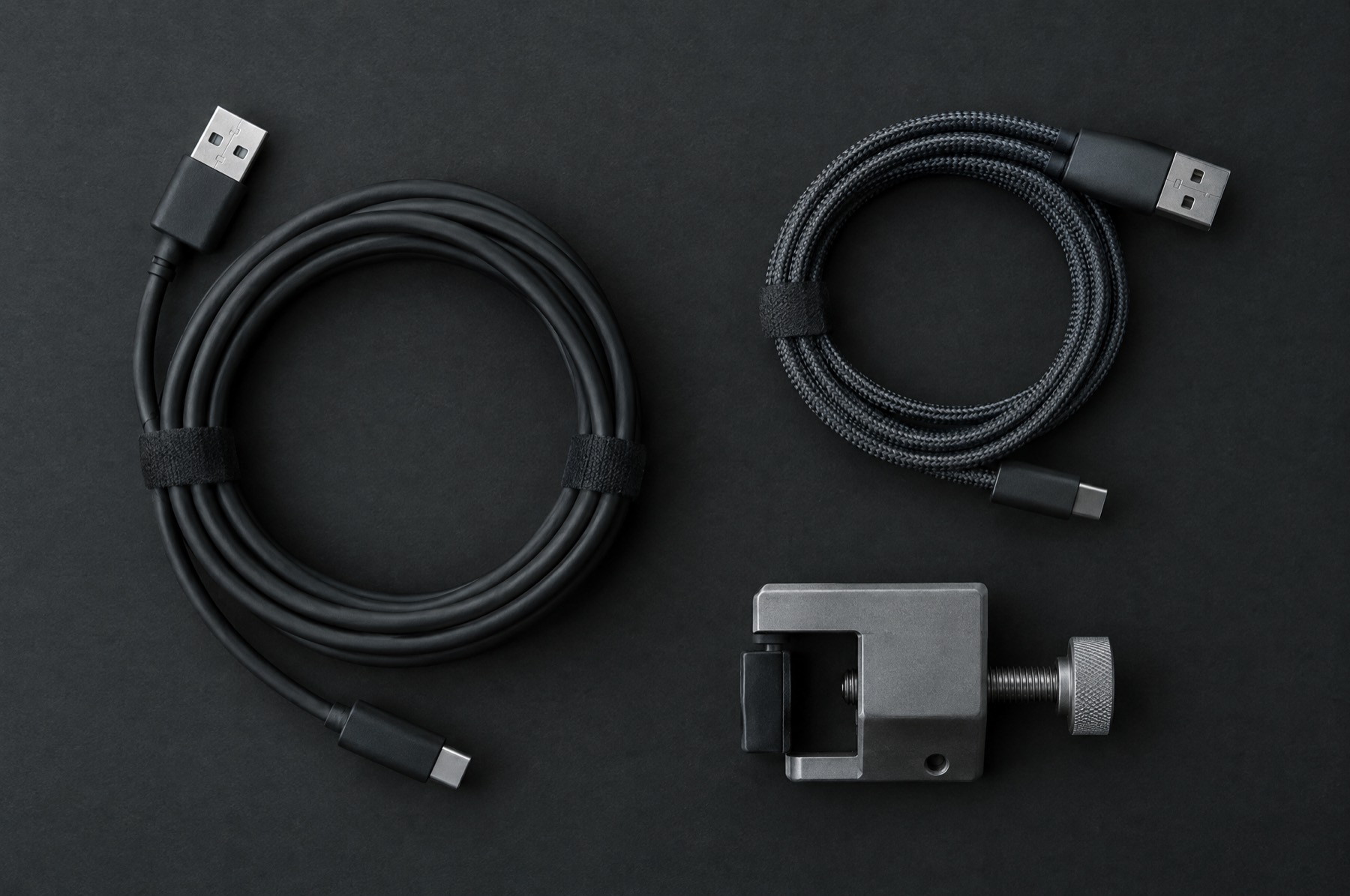 Two coiled cables and a small metal clamp laid out on a dark surface