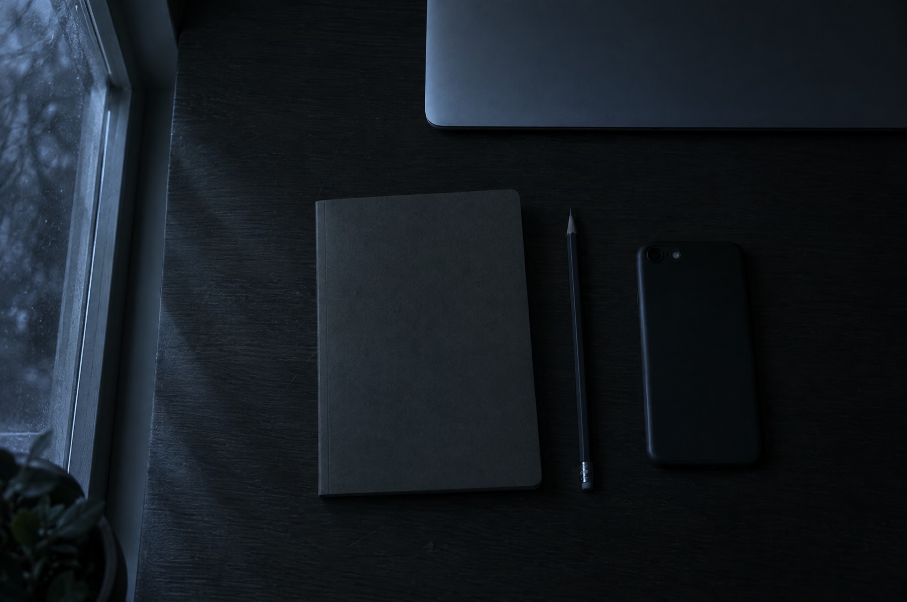 A desk at night: a closed laptop, a notebook, a pencil and a phone lying face down